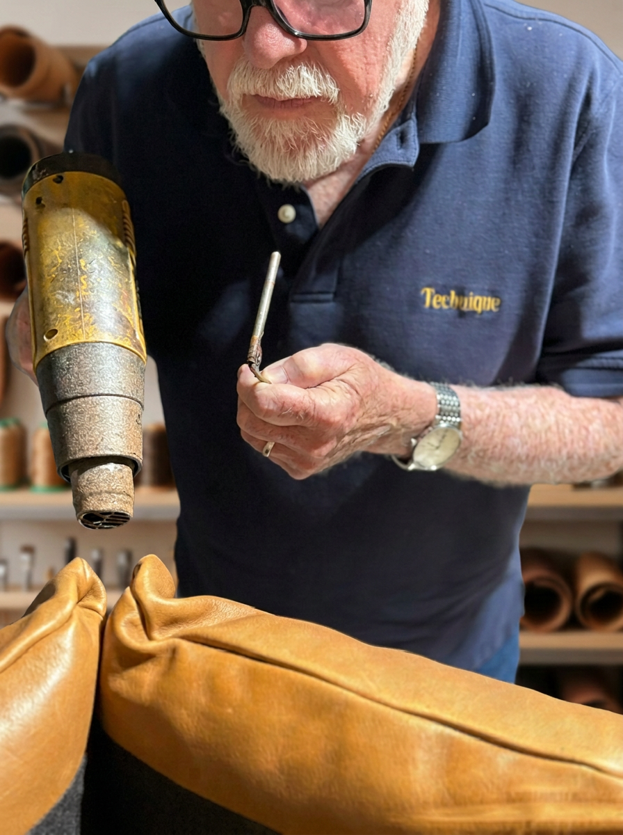 Technique Leather technician repairing a tan leather sofa cushion on site
